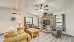 A living room with a sofa, armchair, coffee table, fireplace, TV, and stone wall. - Snowy Peak Views & Cozy Game Nights: Pine Home (Pine)