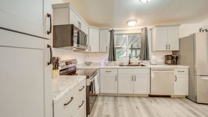 A modern kitchen with white cabinetry, a built-in microwave, a stainless steel refrigerator, and a window with a view of the outdoors. - Snowy Peak Views & Cozy Game Nights: Pine Home (Pine)