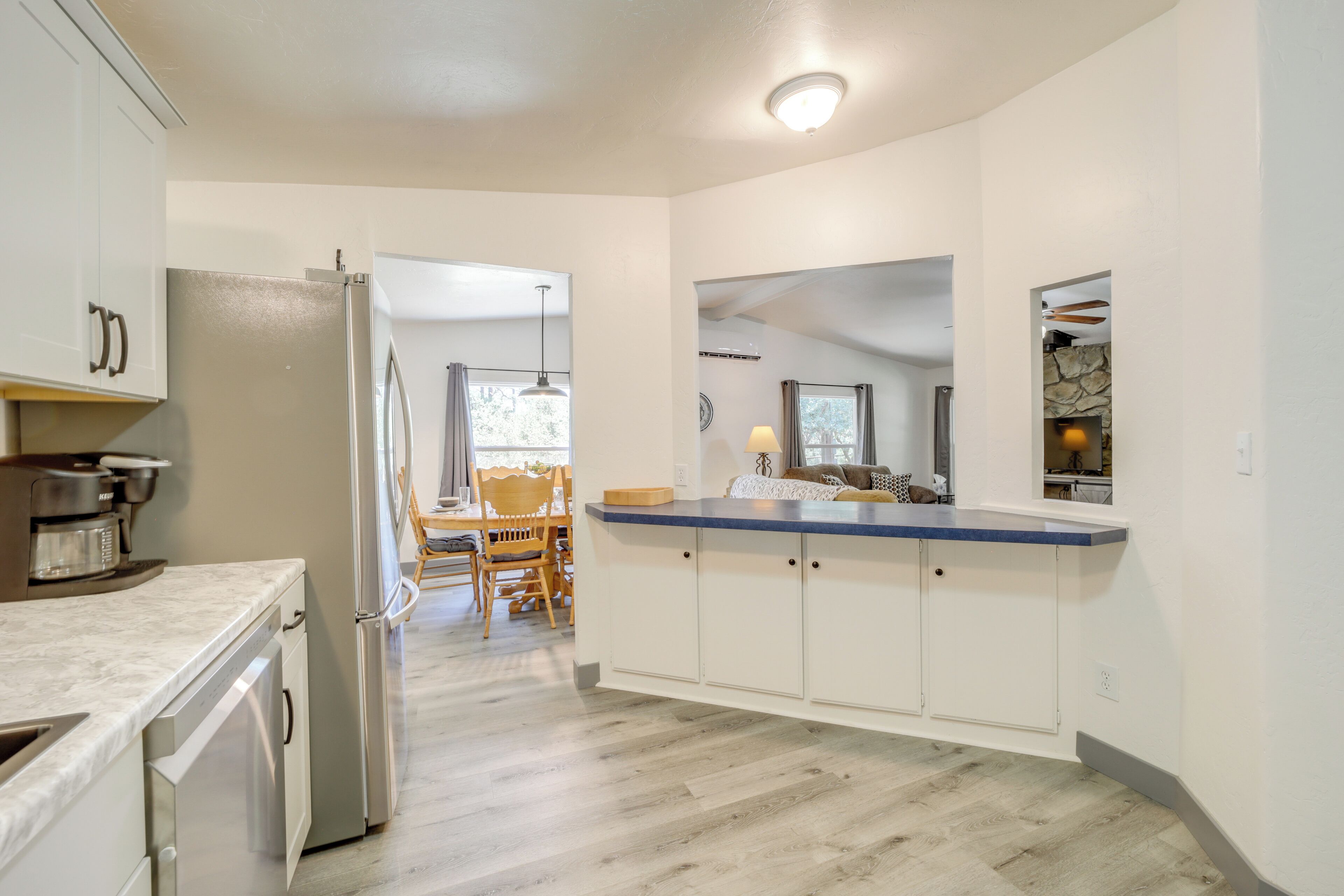 A modern kitchen with white cabinets, a stainless steel refrigerator, and a wooden dining table with chairs.