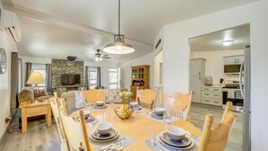 A dining area with a round table set for six, surrounded by wooden chairs. A stone wall and a television are visible in the background. - Snowy Peak Views & Cozy Game Nights: Pine Home (Pine)