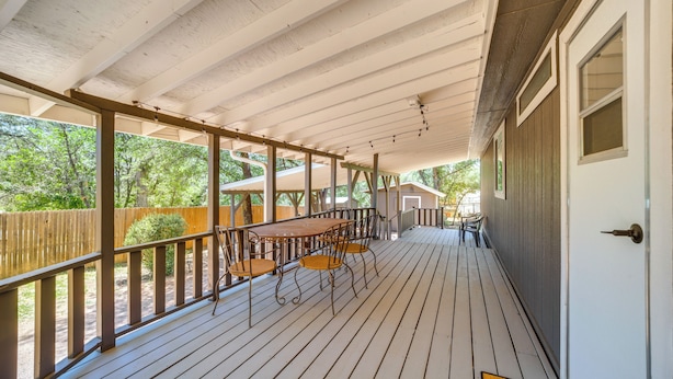 A covered porch with a wooden table and chairs, a wooden railing, and a view of the surrounding greenery. - Snowy Peak Views & Cozy Game Nights: Pine Home (Pine)