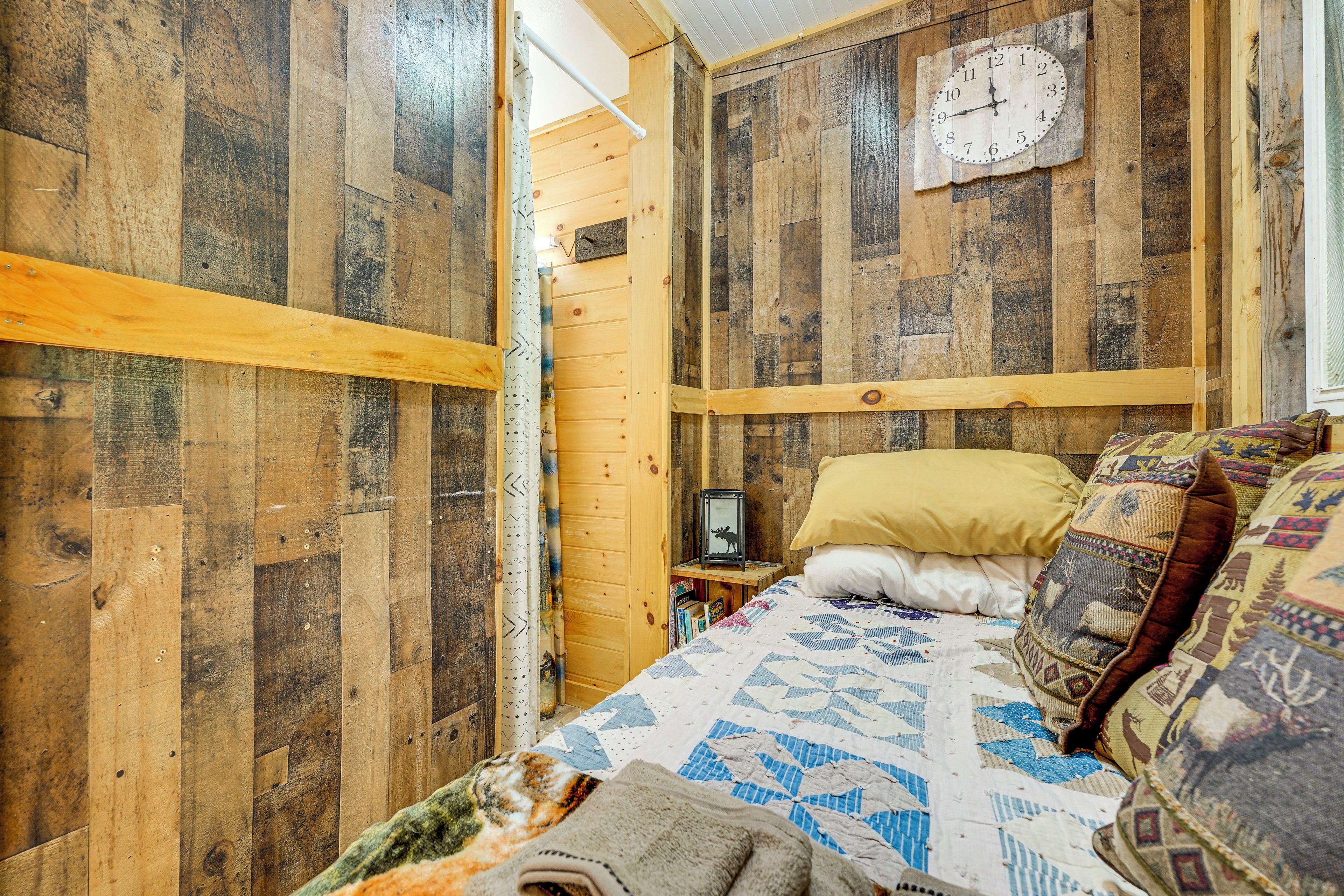 A rustic wooden room with a bed, a clock on the wall, and a small table with a picture frame.