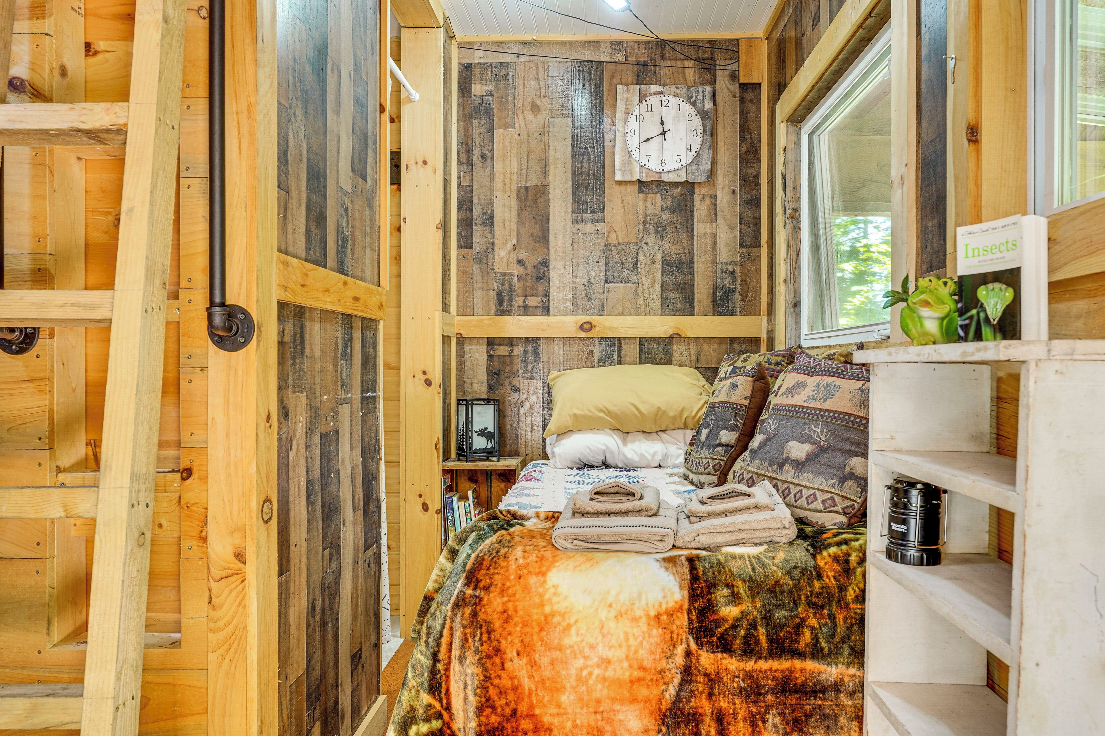 Ein gemütlicher Holzraum mit einem Bett, einer Wanduhr und einem Fenster mit Blick auf Bäume.