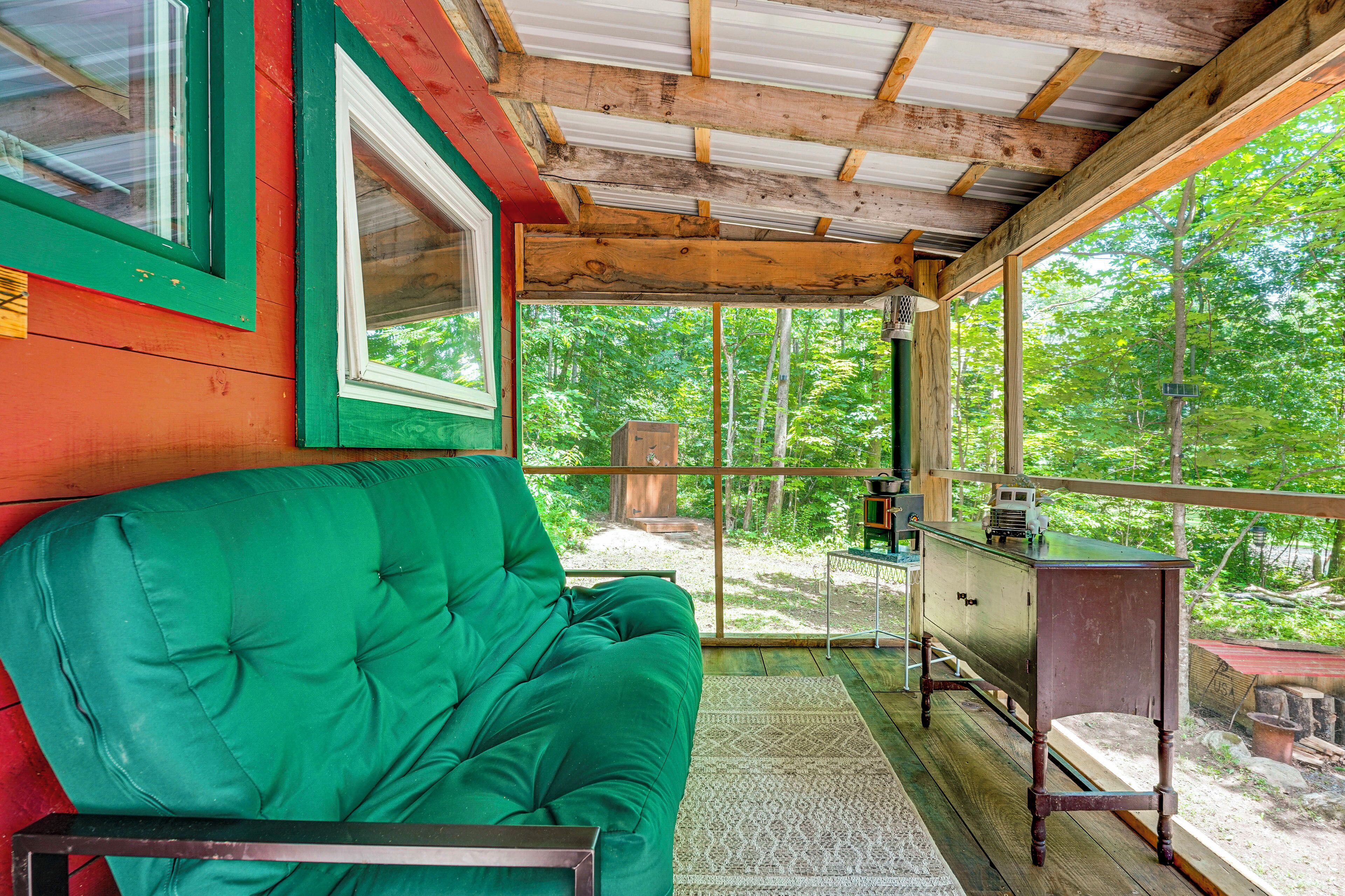 A cozy cabin interior with a green cushioned bench, a wooden table, and a view of the forest through large windows.