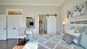 A bedroom with a bed, a chair, a dresser, a mirror, a door, and a bathroom visible through an open door.