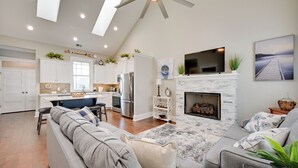 A modern kitchen with white cabinets, a dining area with a bench, a fireplace, and a living room with a sofa and a TV.