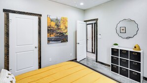Ein Schlafzimmer mit einem Bett, zwei Türen, einem Deckenventilator, einem an der Wand befestigten Regal und einem Gemälde.