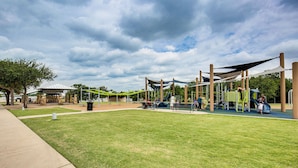 A playground with various play structures, a covered seating area, and a grassy field. - Walk to Lewisville Lake: Dog-friendly Texas Home (Little Elm)