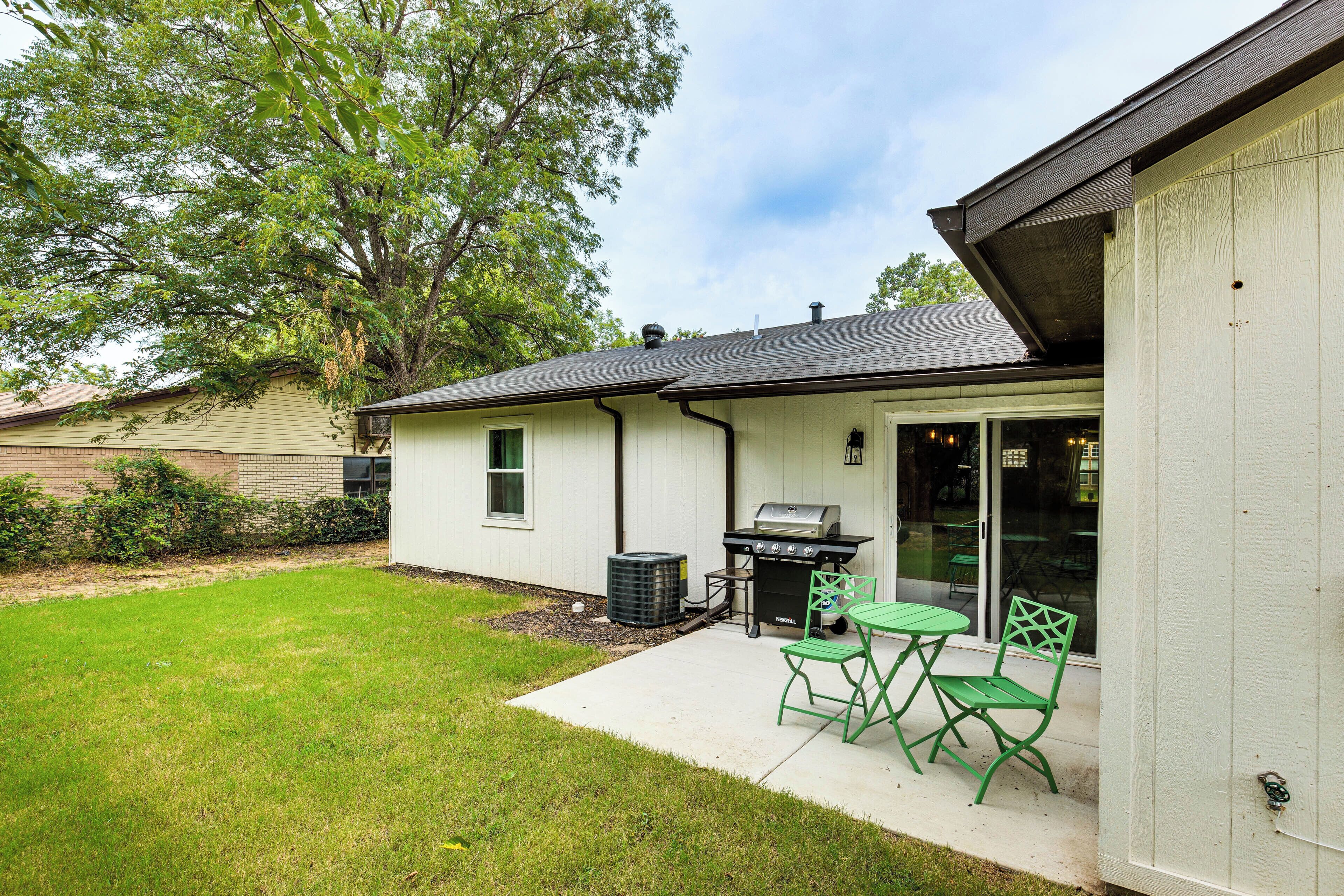 A backyard with a grill, green chairs, and a small table.