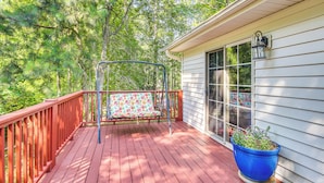A wooden deck with a swing, a potted plant, and a house with a window and a wall-mounted light fixture. - Lovely Mccormick Home in Savannah Lakes Village (McCormick)