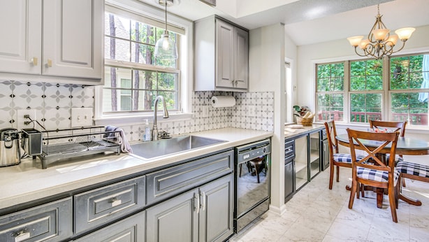 A kitchen with grey cabinets, a large island with a sink, a chandelier, and a dining area with wooden chairs. - Lovely Mccormick Home in Savannah Lakes Village (McCormick)