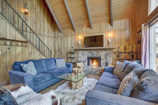 A cozy living room with a stone fireplace, a blue sofa, and a glass coffee table. - Chic Lake Arrowhead Retreat: 4 Seasons of Fun! (Lake Arrowhead)