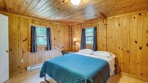 A wooden-paneled bedroom with a bed, two windows with curtains, a nightstand with a lamp, and a ceiling light. - Clarkson Cabin - 17 Mi to Mammoth Cave Natl Park! (Clarkson)