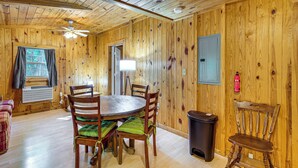 A wooden-paneled room with a round table and chairs, a ceiling fan, a window with curtains, and a fire extinguisher on the wall. - Clarkson Cabin - 17 Mi to Mammoth Cave Natl Park! (Clarkson)