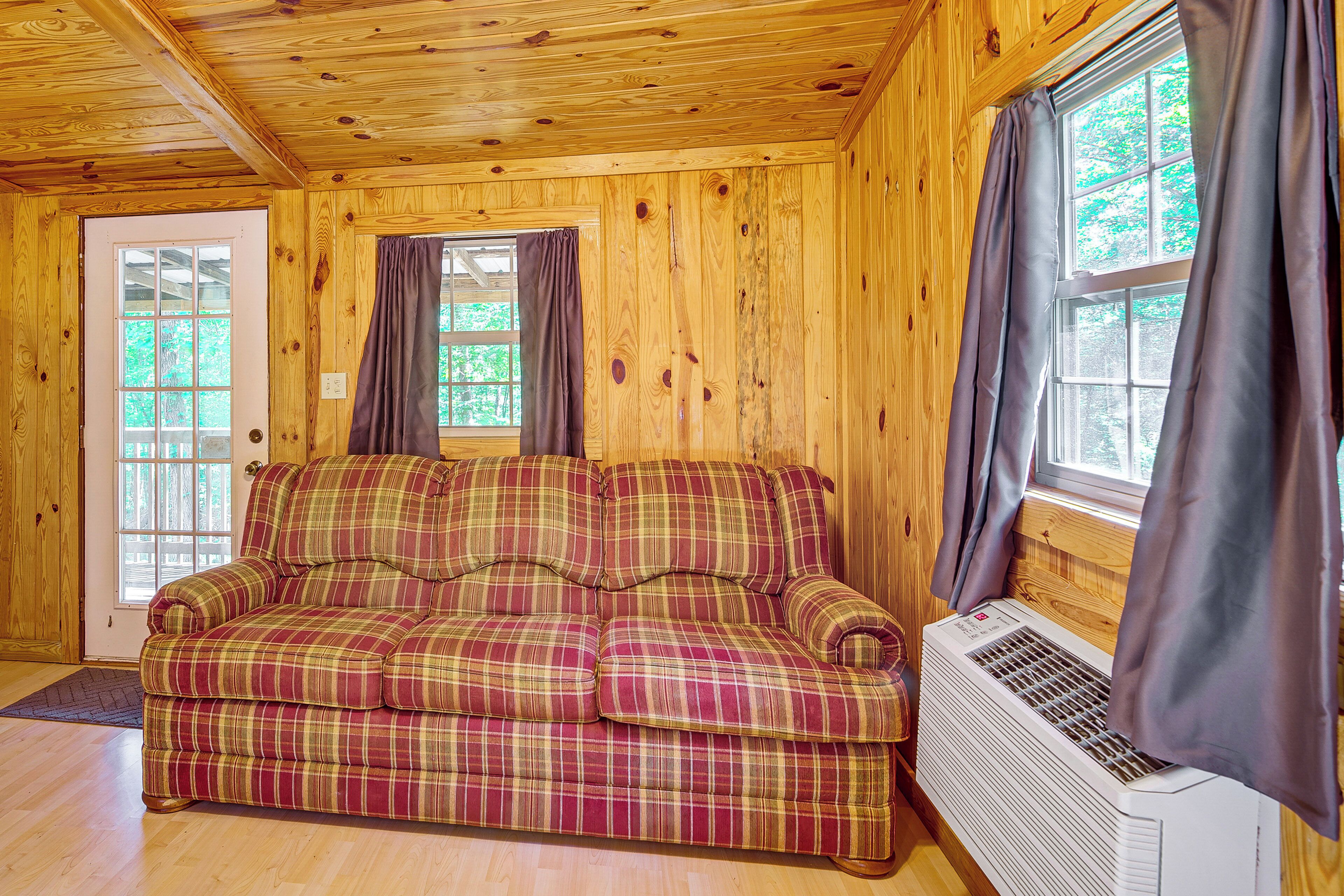 Ein Holzblockhaus-Innenraum mit einem Sofa mit Karomuster, einer Tür und einem Fenster mit Vorhängen.