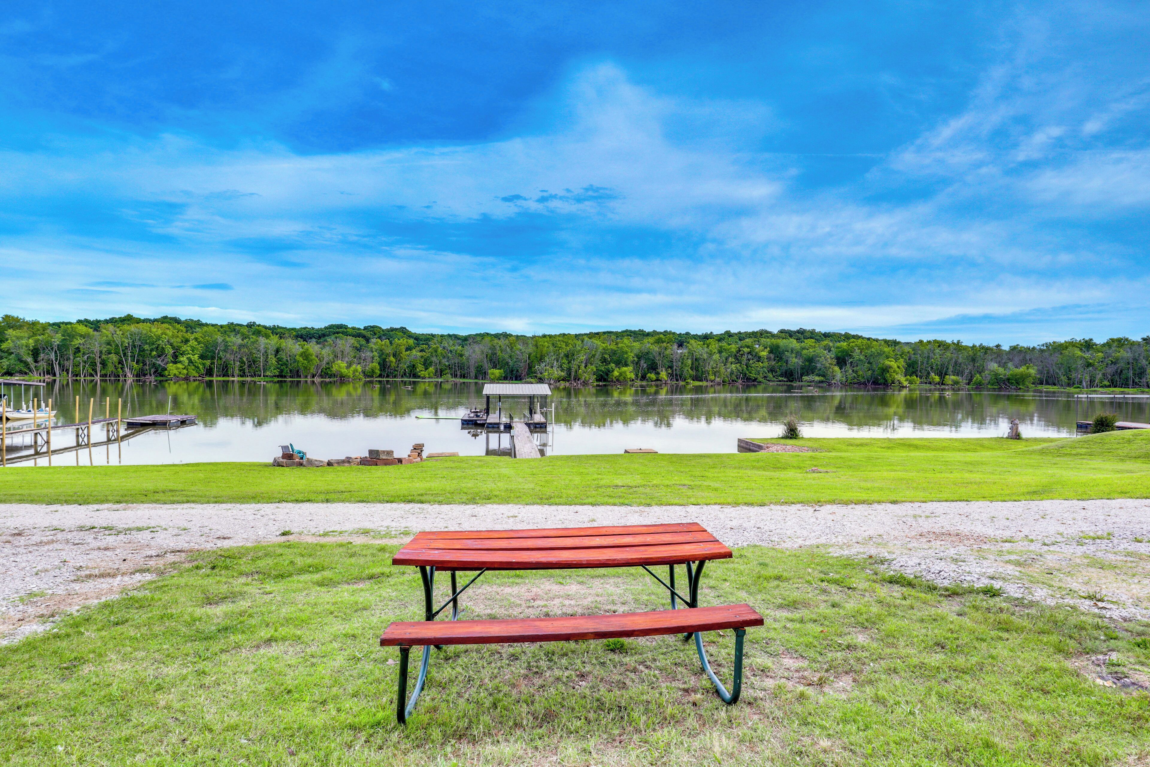 A picnic table in a grassy area with a lake and dock in the background.