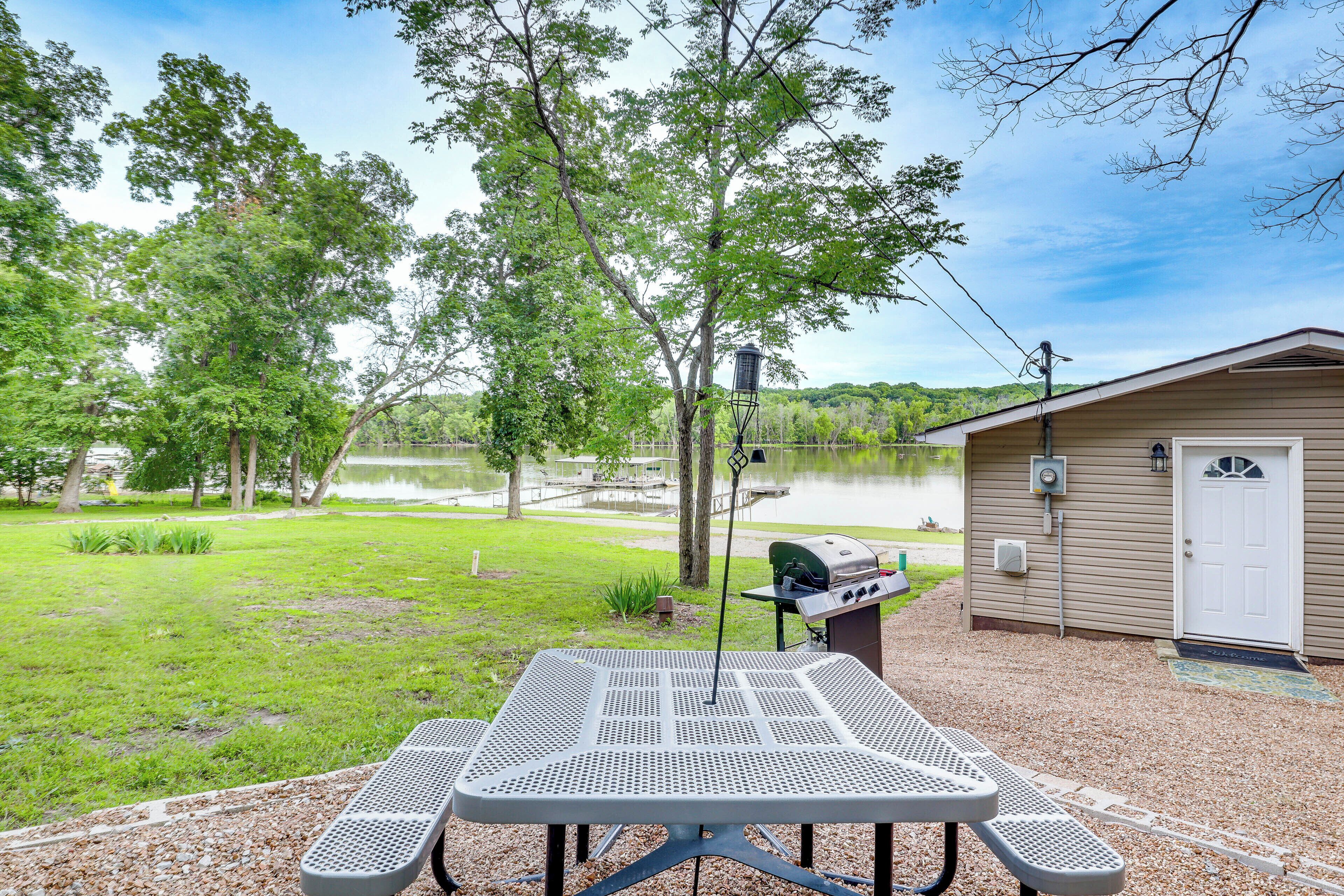 A picnic table with a grill, a small shed, and a lake in the background.