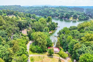 An aerial view of a lakeside property with dense forestation, a small building with a red roof, and boats on the water. - Smith Mountain Lake Cottage w/ Dock + Fire Pit! (Glade Hill)