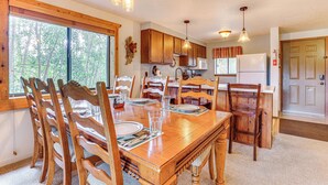 Un coin repas avec une table en bois, dressée pour quatre personnes, entourée de chaises en bois. On trouve des placards en bois au-dessus de la table et un réfrigérateur blanc sur la droite.