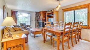 Un salon chaleureux avec une cheminée, des meubles en bois et de grandes fenêtres donnant sur l’extérieur.