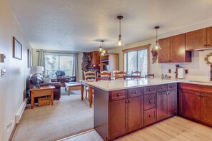 A kitchen with wooden cabinets, a central island, pendant lights, and a dining area with a table and chairs.