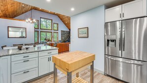 A modern kitchen with white cabinets, a stainless steel refrigerator, a wooden table, and a stone backsplash. - Near Hiking Trails & Ski Resorts: Killington Home! (Killington)