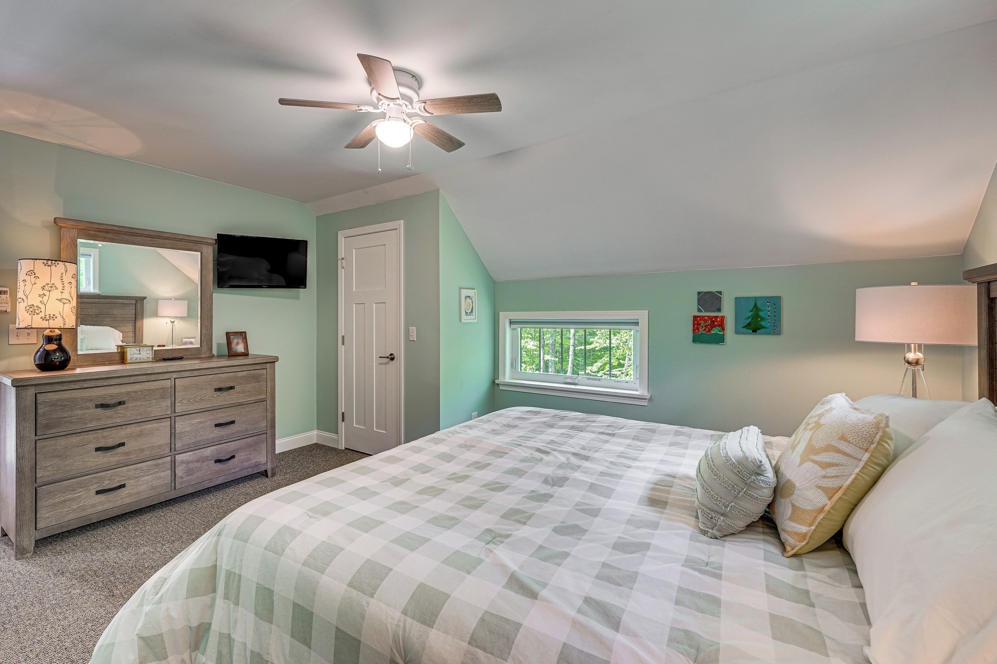 A bedroom with a bed, dresser, ceiling fan, window, and artwork on the walls.
