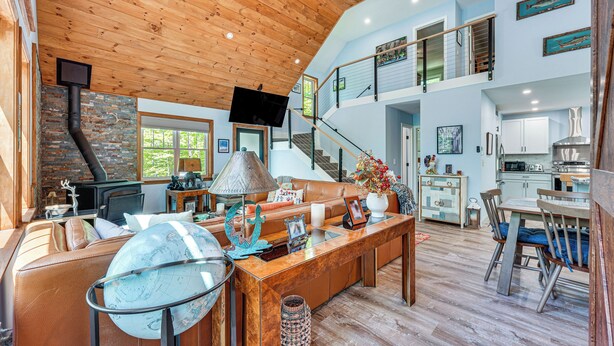 A spacious living area with a wooden ceiling, a large globe, a fireplace, and a kitchen in the background. - Near Hiking Trails & Ski Resorts: Killington Home! (Killington)