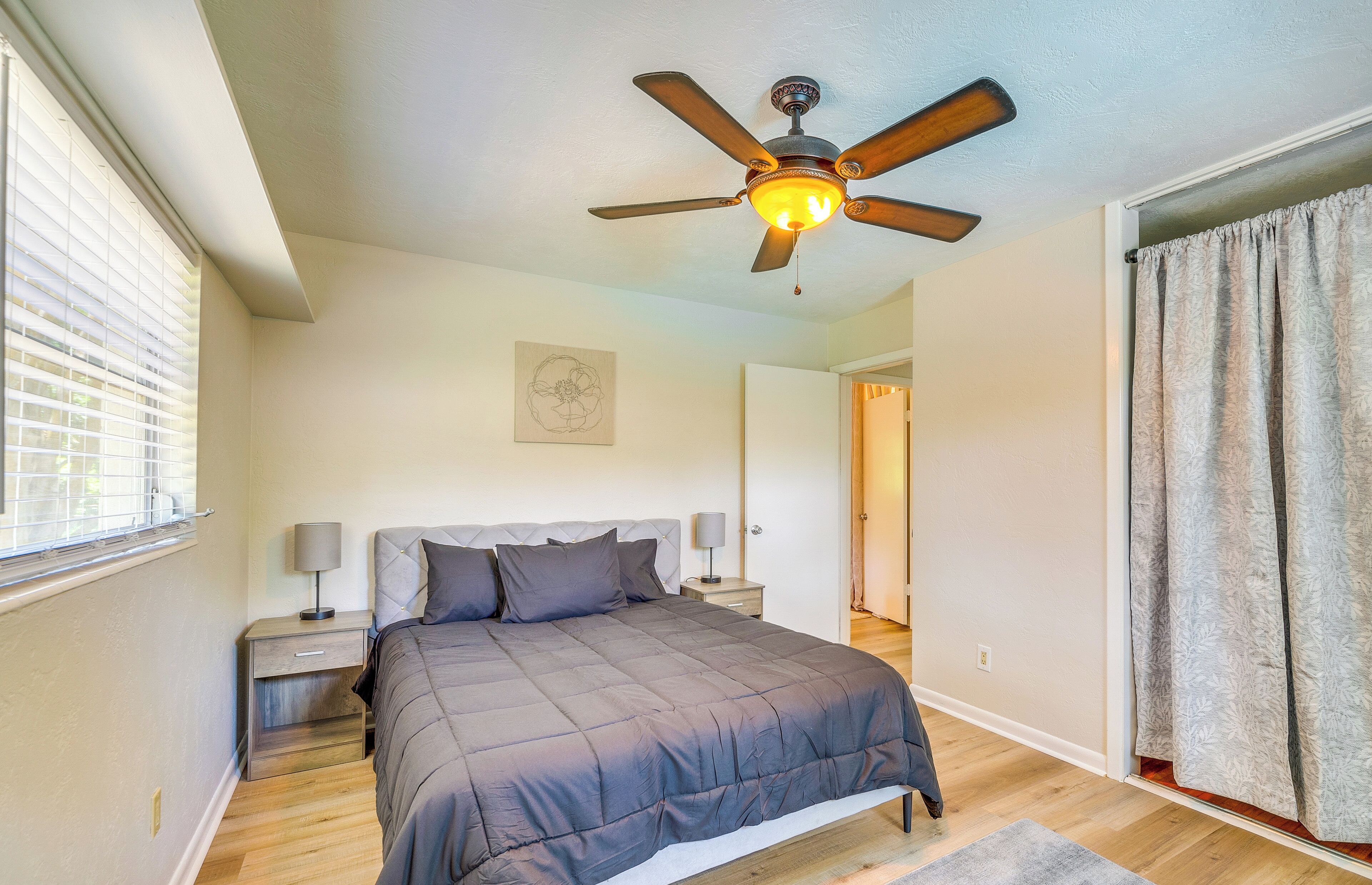 Une chambre à coucher avec un lit, des tables de chevet, un ventilateur de plafond et une fenêtre avec des stores.