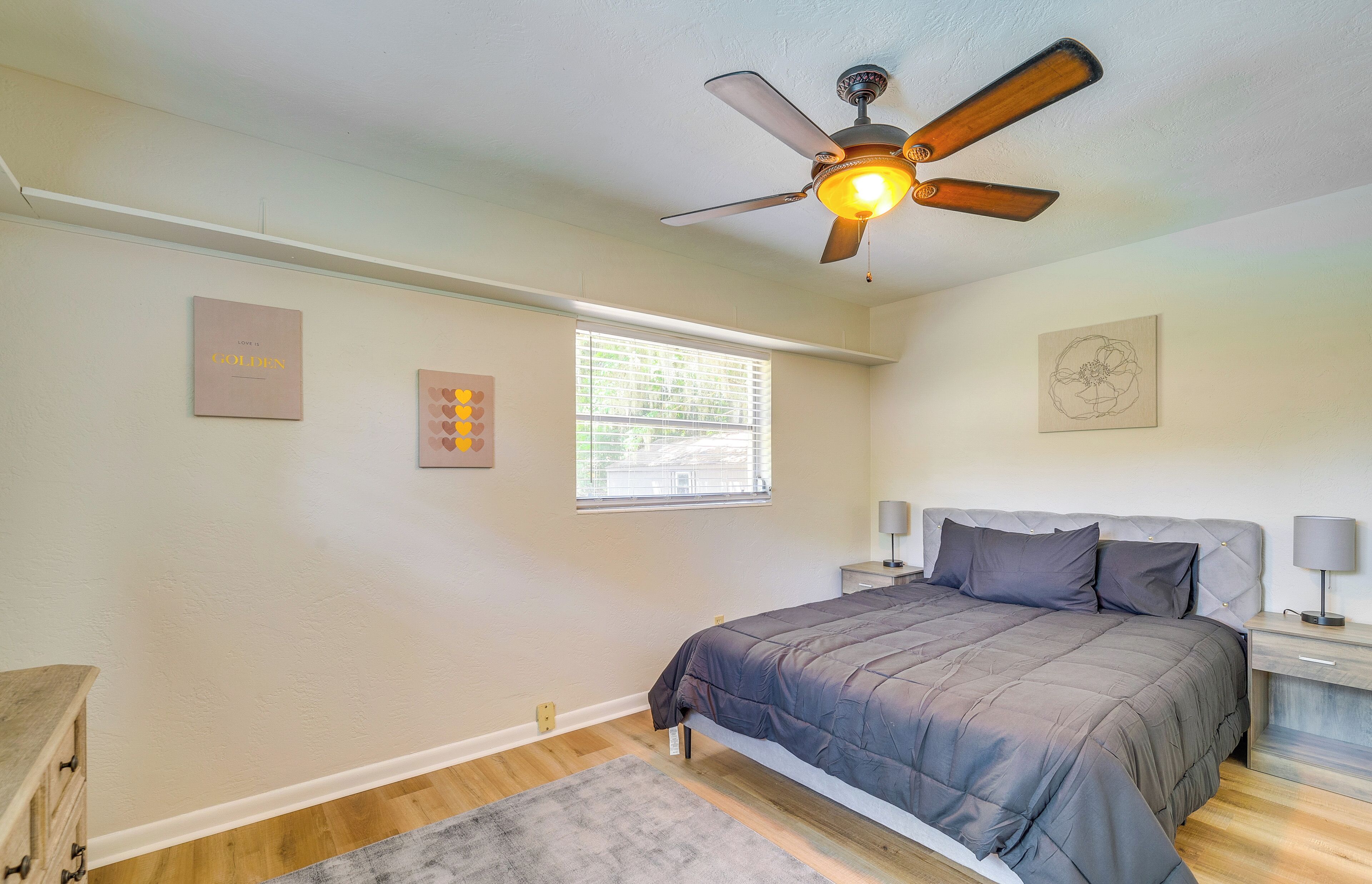 Un dormitorio con cama, ventilador de techo, ventana y decoración en la pared.