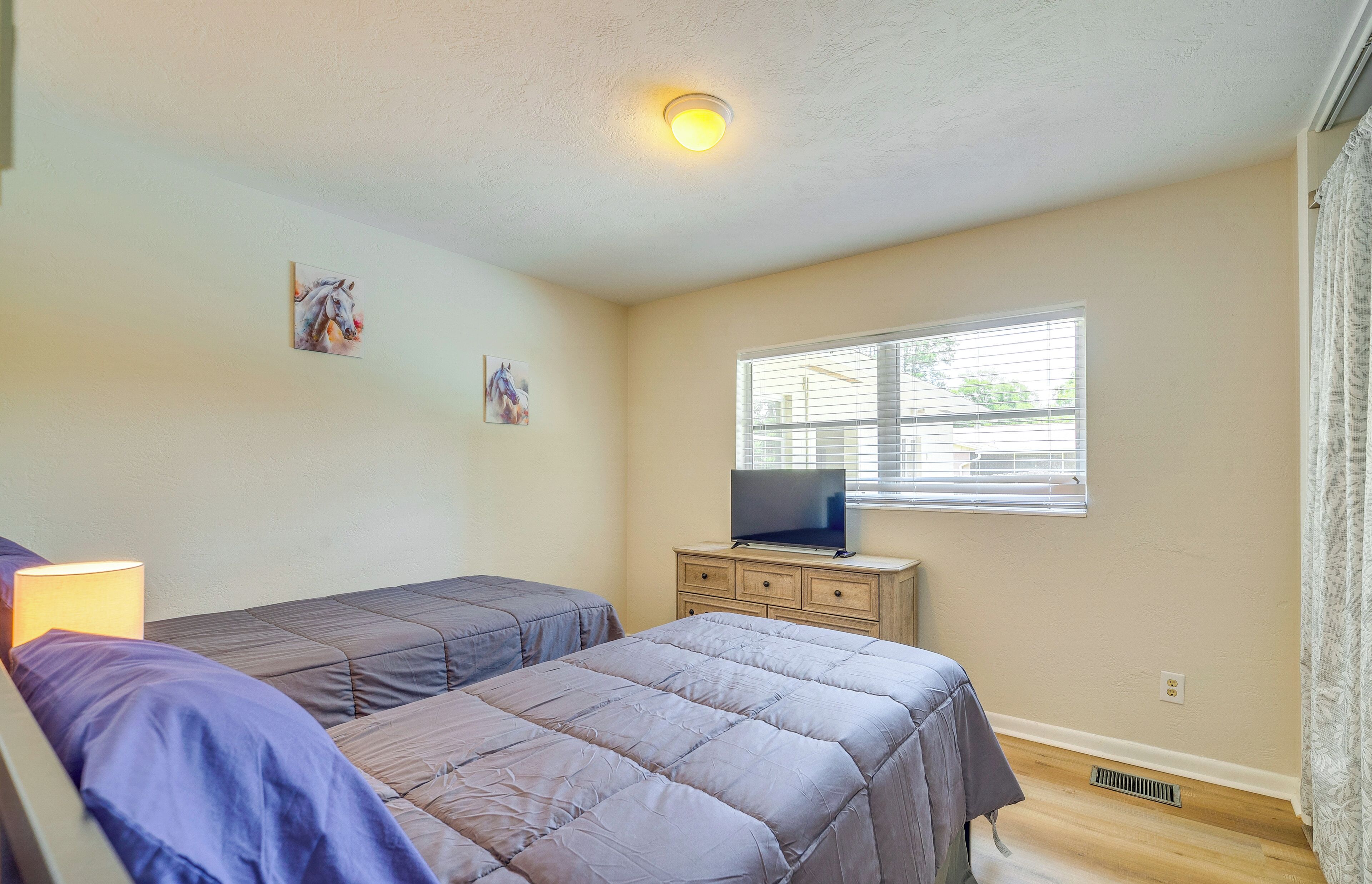 A bedroom with two beds, a dresser, a television, and a window with blinds.