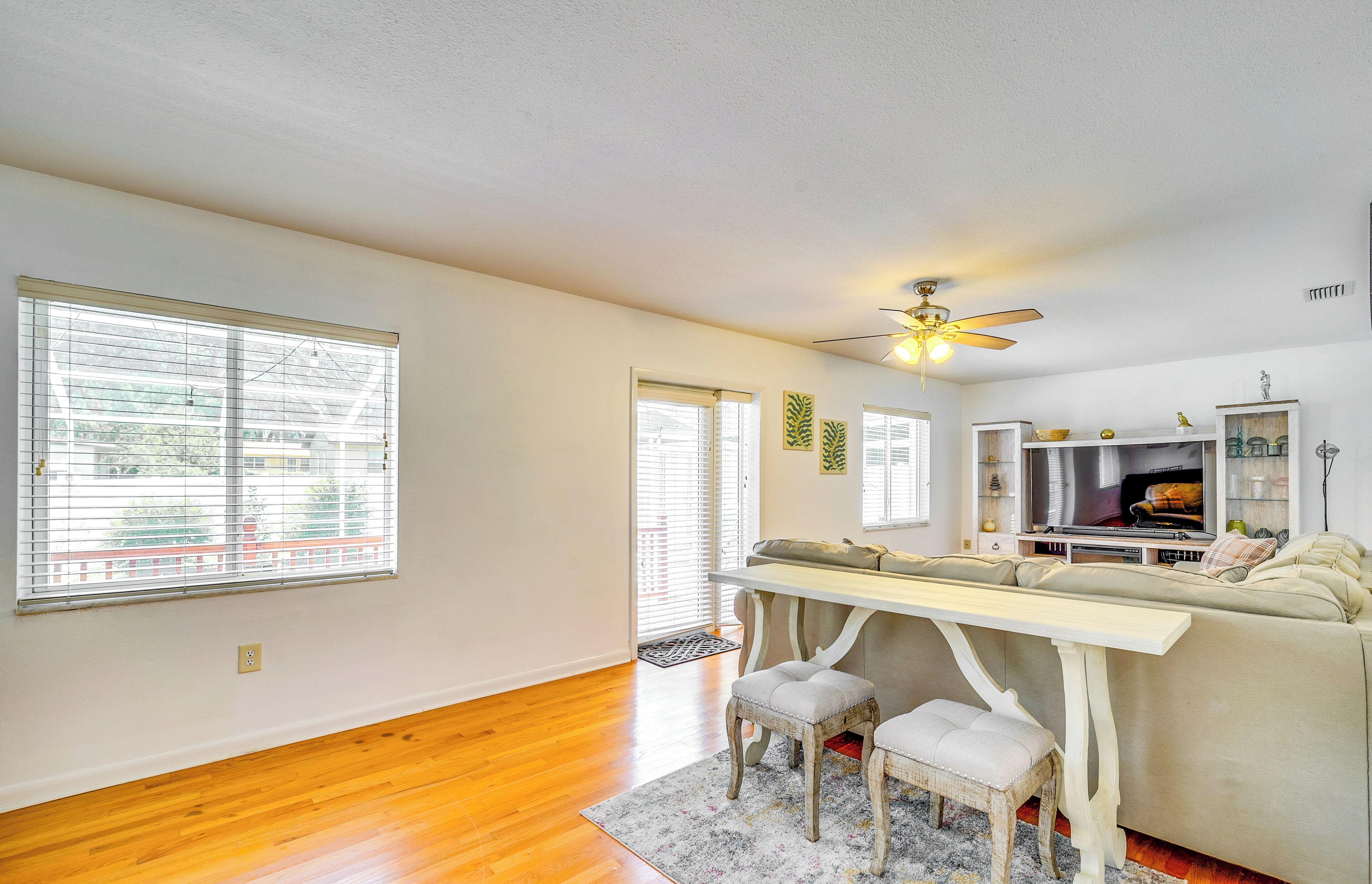 A spacious living room with hardwood floors, a sofa, a coffee table, and a ceiling fan.
