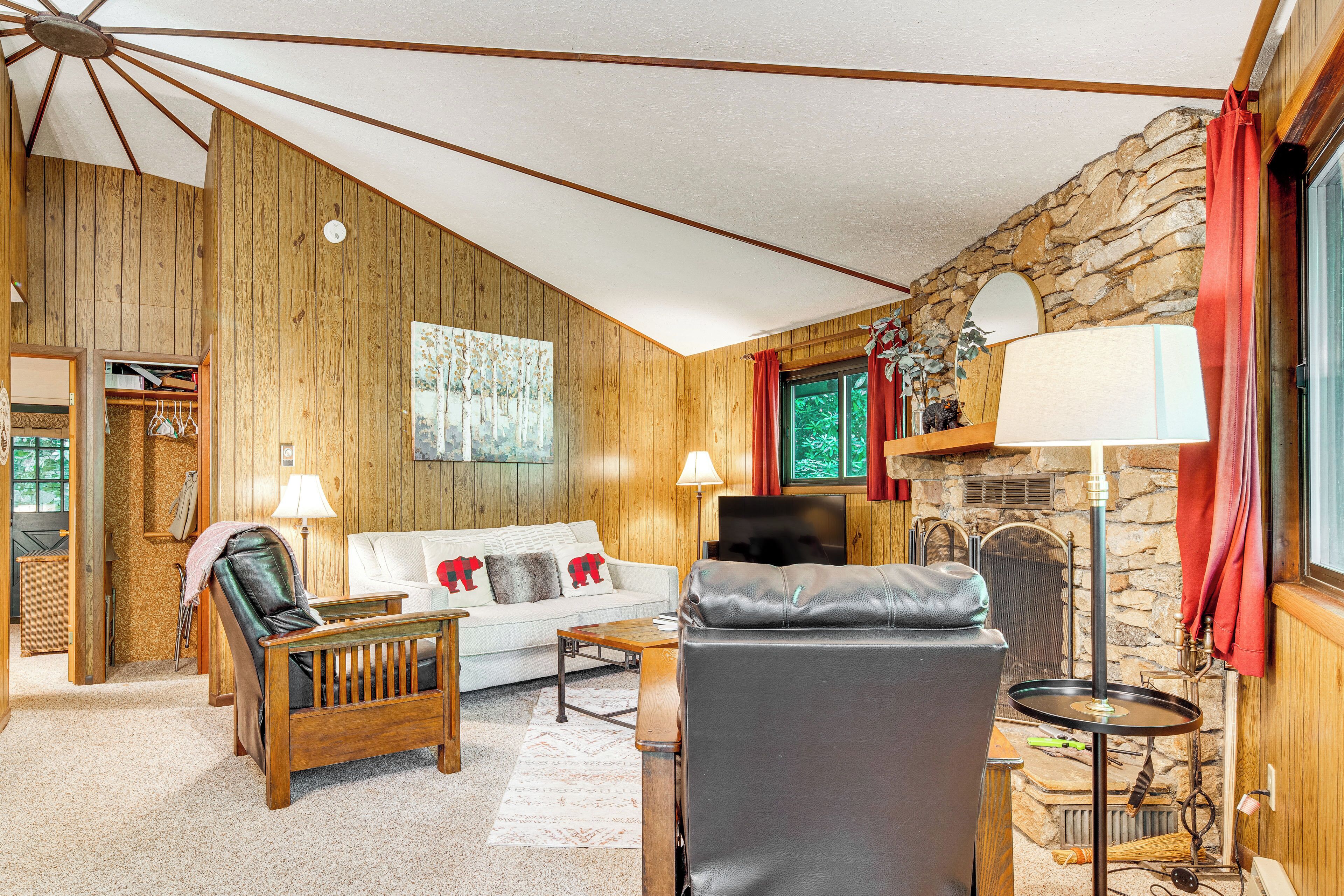 Una sala de estar acogedora con paredes de madera, chimenea de piedra, sofá, sillón de cuero y televisor.