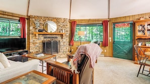 A cozy living room with a stone fireplace, wooden furniture, and a television. - 'the Round House' - Treetop North Carolina Cabin! (Hendersonville)