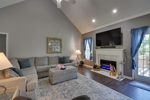 A living room with a sofa, ottoman, TV, fireplace, and a decorative piece on the mantel. - Unicoi Wine Trail Retreat! Bbq-ready Deck w/ Views (Sautee Nacoochee)
