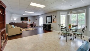 A spacious living room with a large sofa, a dining table with chairs, and a television mounted on the wall. - Wine Trail Apt 7 Mi to Yonah Mtn! Patio & Views (Sautee Nacoochee)