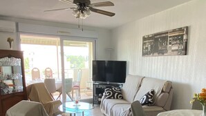 A living room with a sofa, armchairs, a TV, a ceiling fan, and a dining table. - 4-person air-conditioned apartment with beach and all amenities within walking distance (Saint-Raphaël)