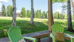 Een overdekt buitengebied met twee groene Adirondack-stoelen en een houten bank.
