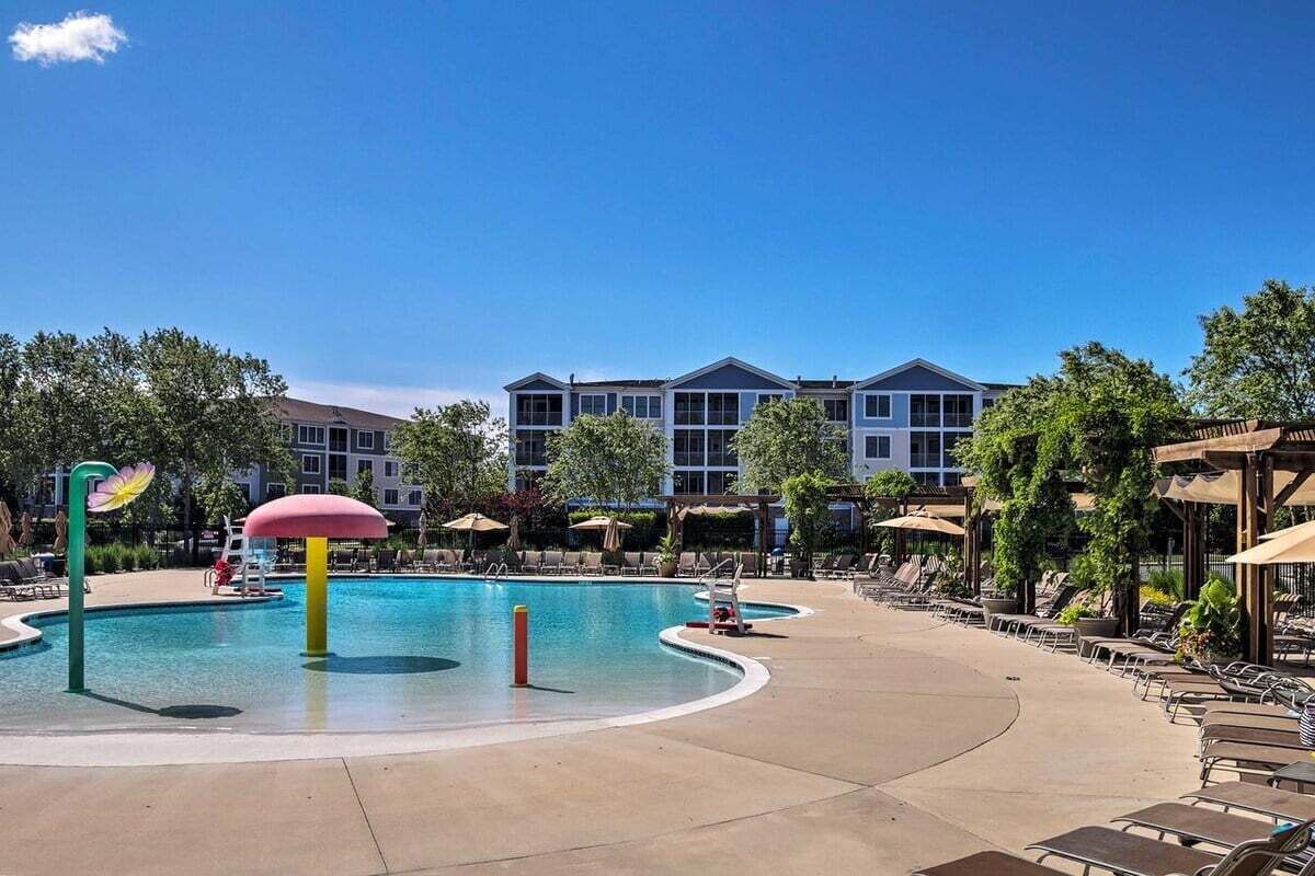 A swimming pool with lounge chairs and umbrellas, surrounded by trees and a building in the background.