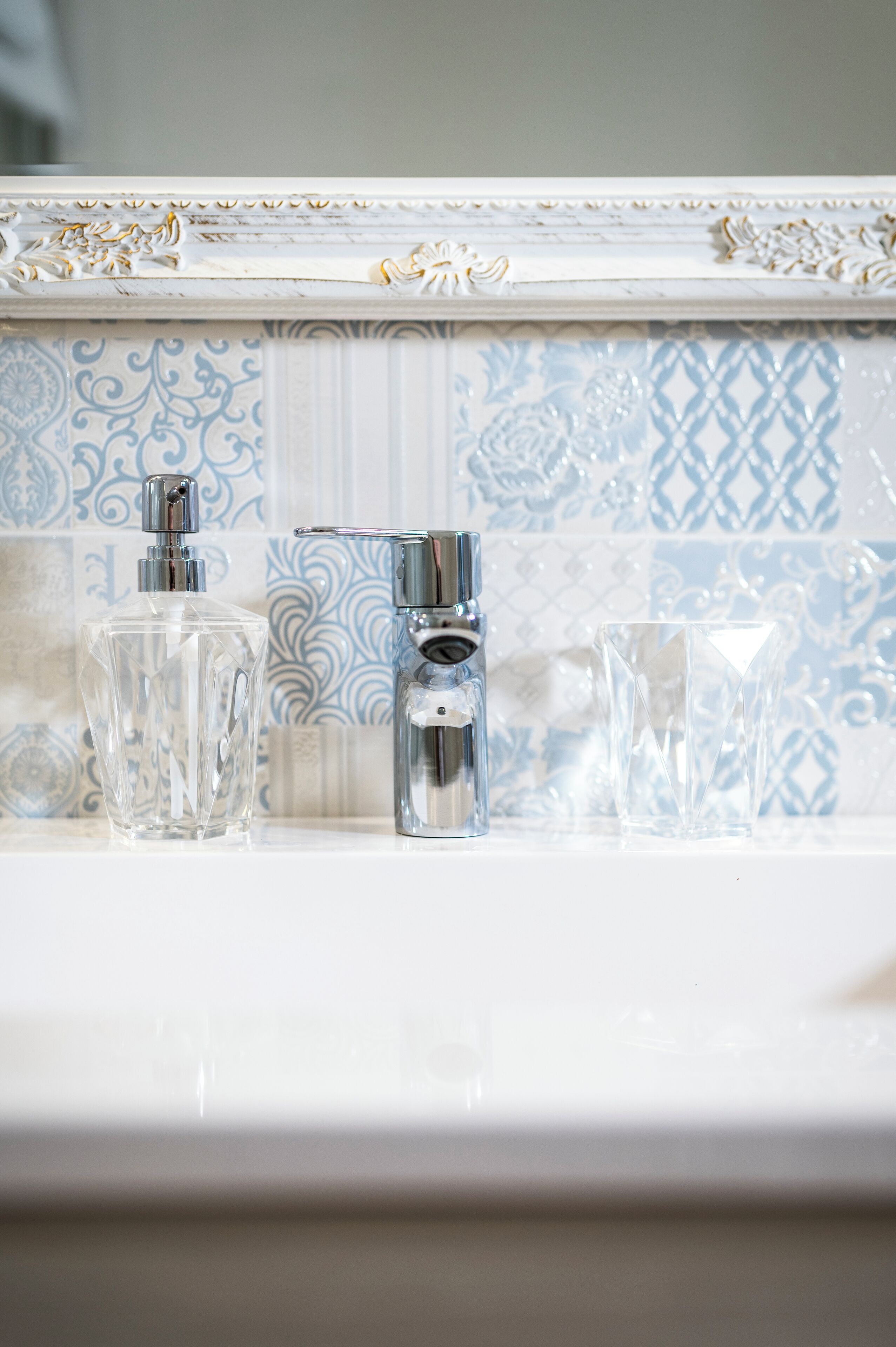 A bathroom with a white sink, a chrome faucet, and a clear glass bottle.