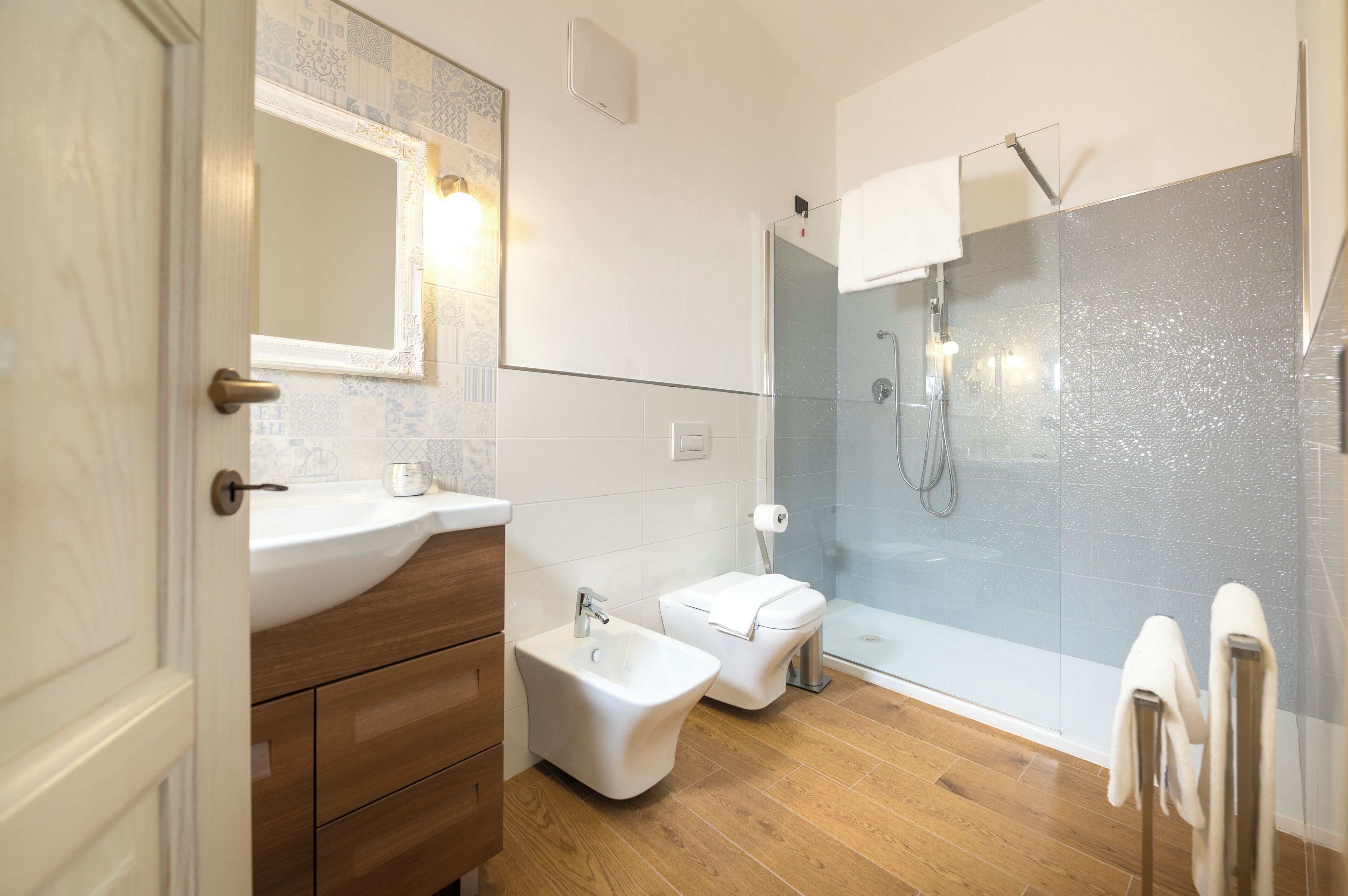Une salle de bain moderne avec un meuble-lavabo en bois, un bidet, des toilettes et une douche séparée par une paroi de verre.