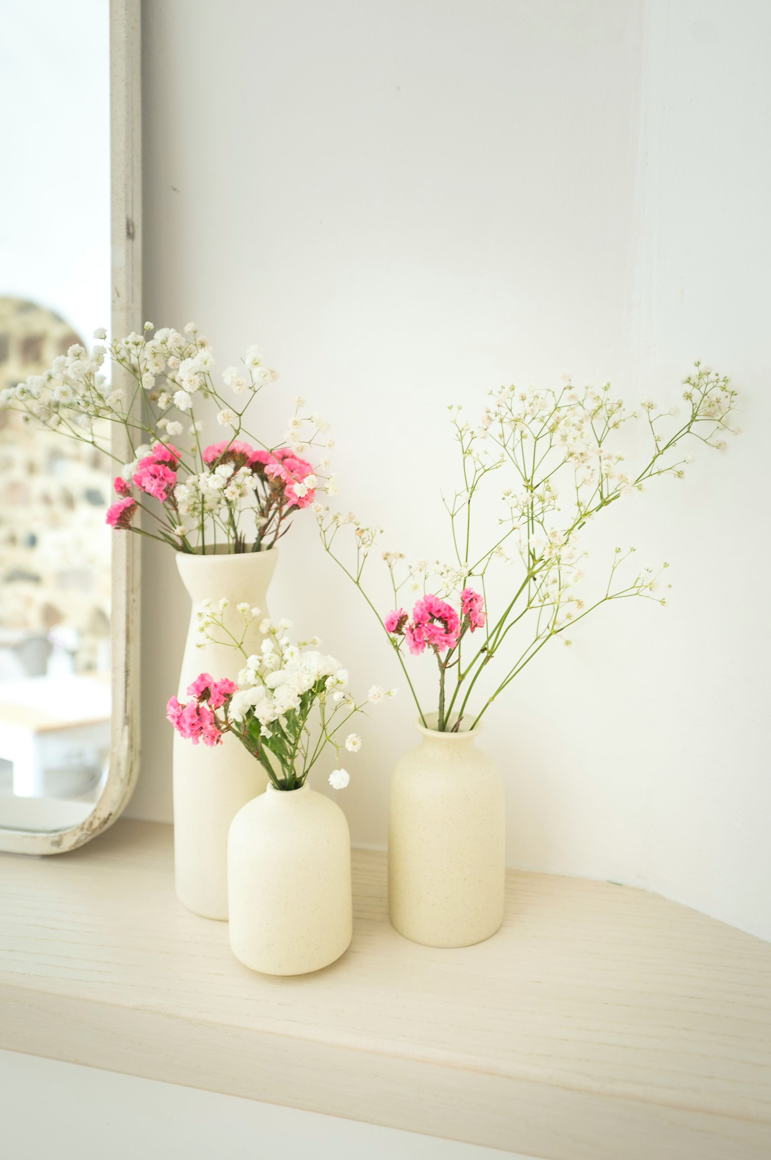 Tres jarrones con flores sobre una repisa junto a una ventana.