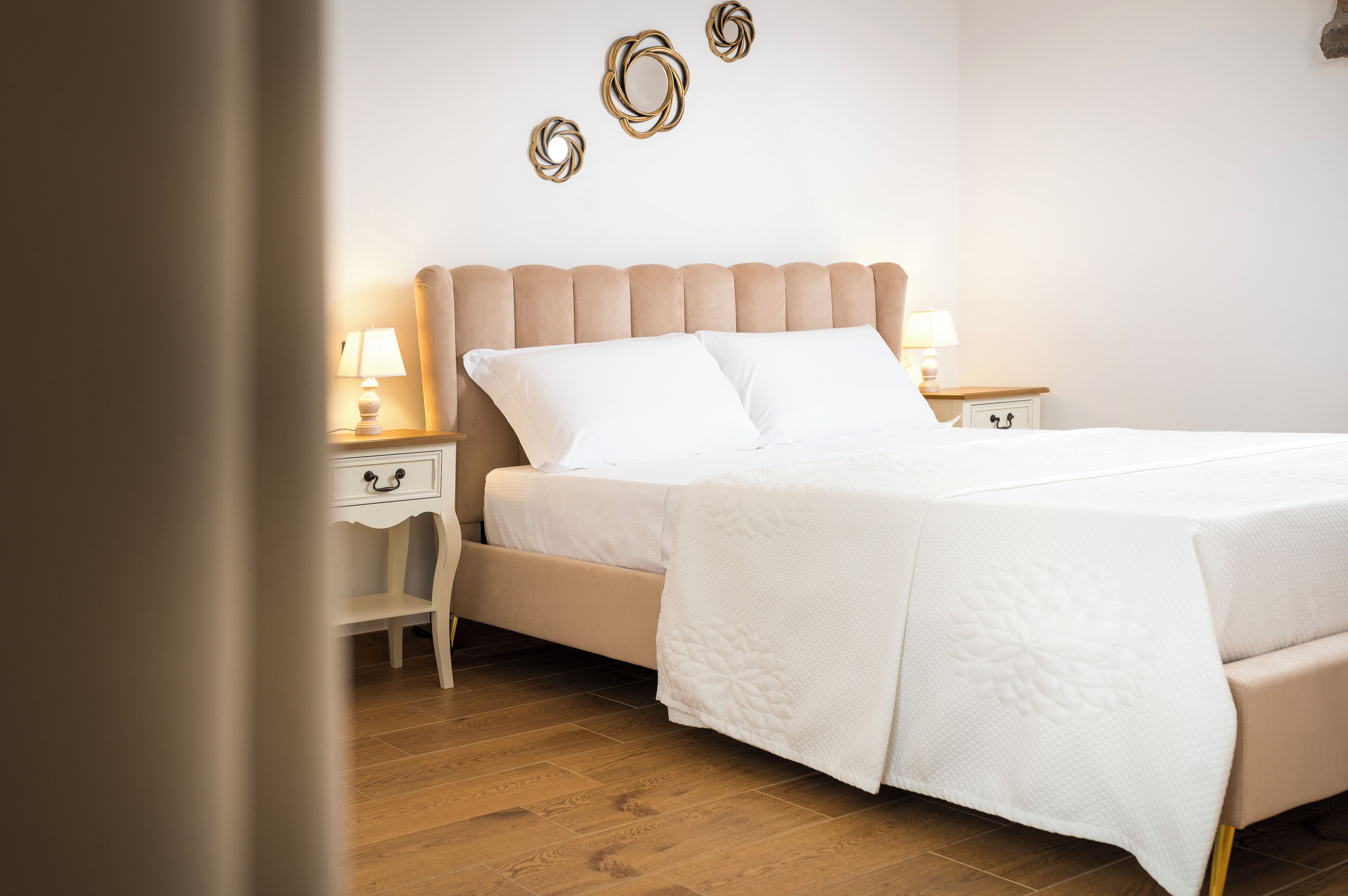 Un letto ben rifatto con copripiumino e cuscini bianchi, un comodino in legno con una lampada, e una parete decorata con tre elementi murali circolari.