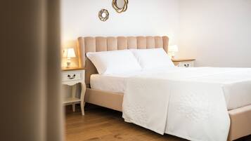 Una cama bien hecha con una colcha blanca y almohadas, una mesita de noche de madera con una lámpara, y una pared decorada con tres piezas de arte circular.