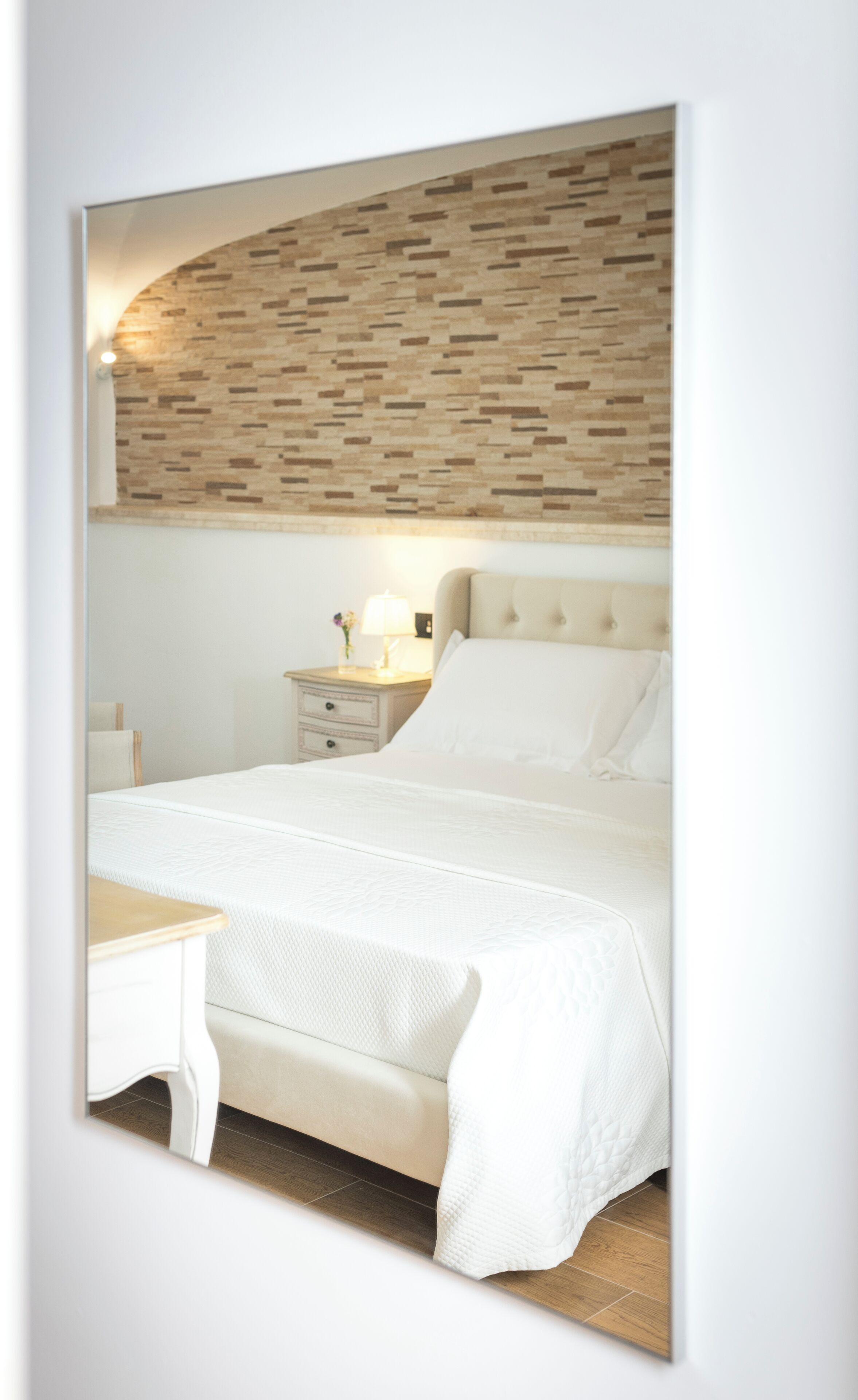 Een slaapkamer met een bed, nachtkastje, lamp en een muur met een baksteenmotief.