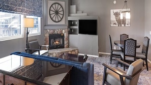 A living room with a fireplace, a TV, a dining area with chairs, and a view of a building outside.