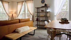 Ein gemütliches Wohnzimmer mit braunem Ledersofa, einem Holztisch, einem Esstisch mit Stühlen und einem Bücherregal.