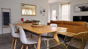 Ein modernes Wohnzimmer mit einem Holzesstisch, weißen Stühlen, einem braunen Ledersofa und einem Wand-Fernseher.