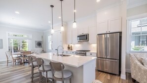 A modern kitchen with white cabinetry, stainless steel appliances, and a central island with bar stools. - *New* Seabrook's Happy Place: Dog Friendly! (Pacific Beach)