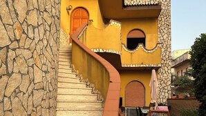 Un edificio de varios niveles con muros de piedra y revestimiento de yeso, y una escalera curva que lleva a una puerta.